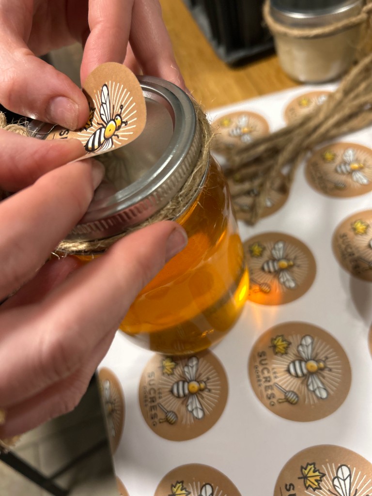 Pose d'une étiquette d'abeille sur un pot de miel Les Sucres Dorés